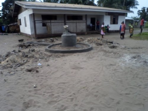 A photo showing the position of the hand pump in front of the school building