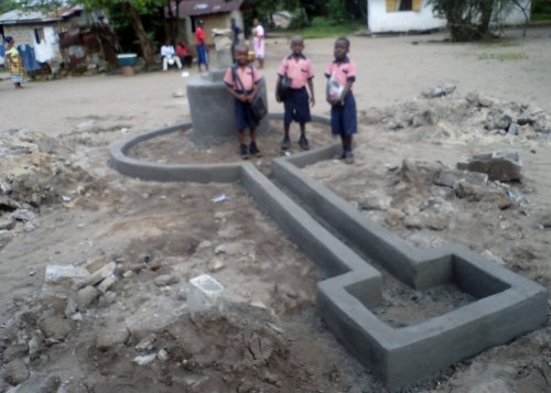 Three kindergarten kids posing at the newly renovated hand pump